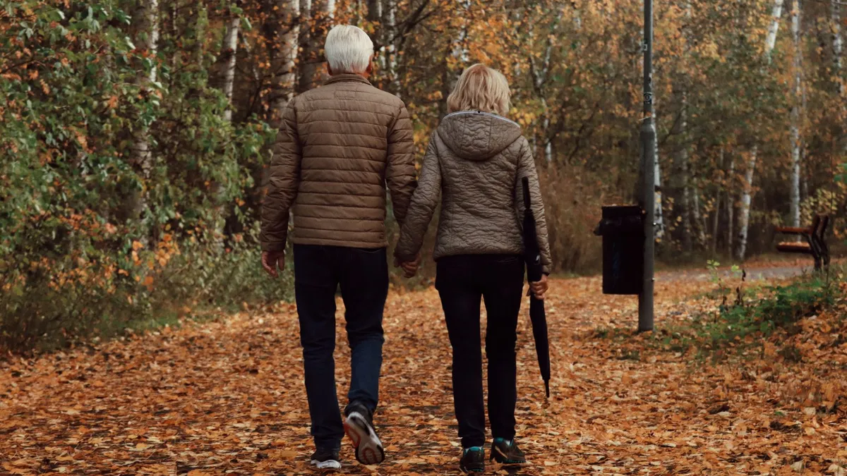 An elderly couple walking outdoors together in autumn